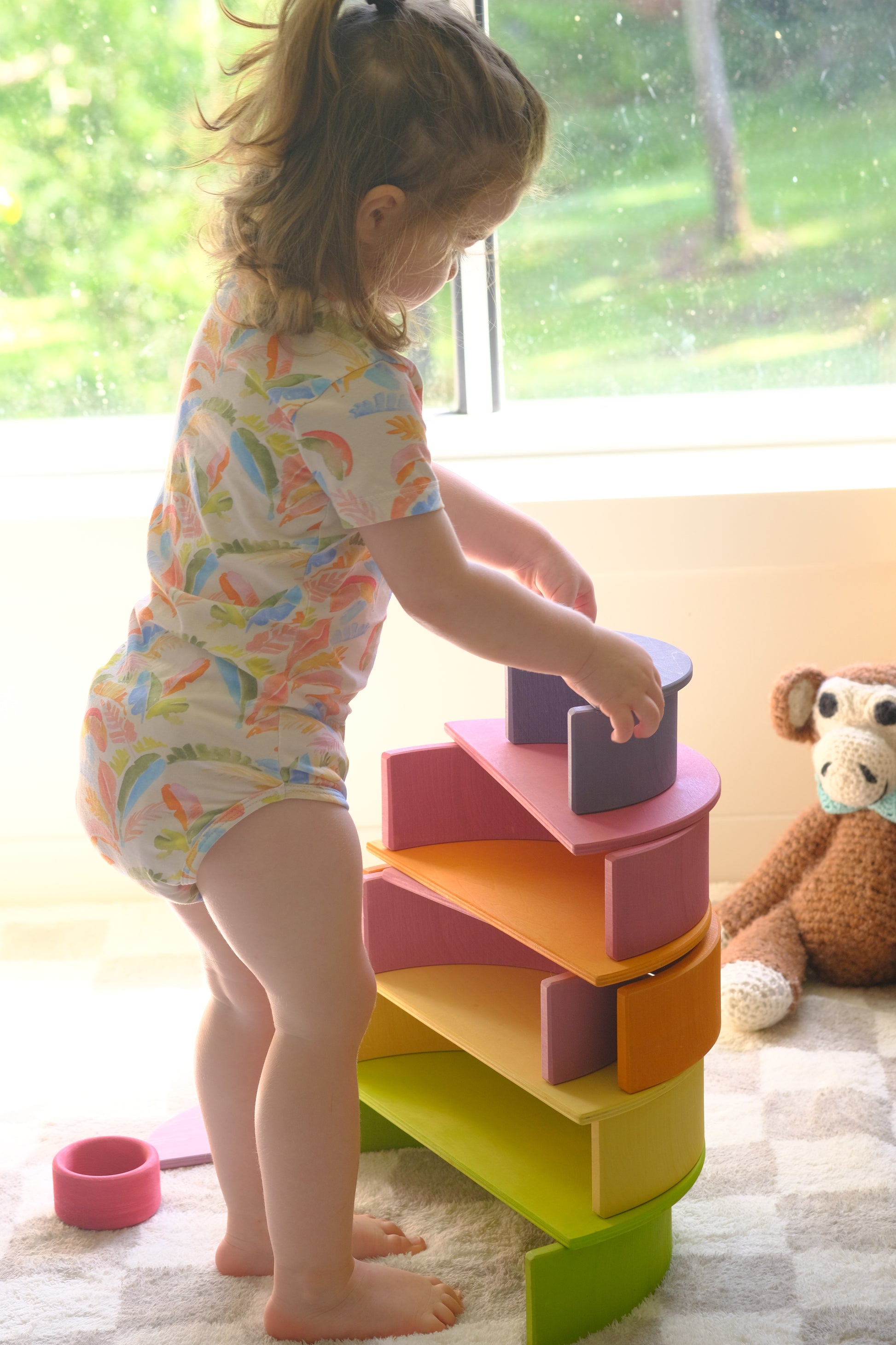 Child playing with colorful wooden rainbow  steps near a window